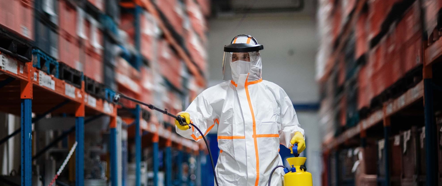 Man worker with protective mask and suit disinfecting industrial factory with spray gun_
