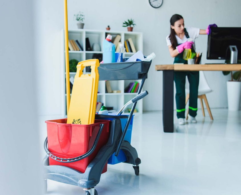 Young female janitor cleaning office with various cleaning equipment
