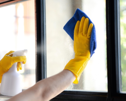 Close up of a person in yellow gloves cleaning a window