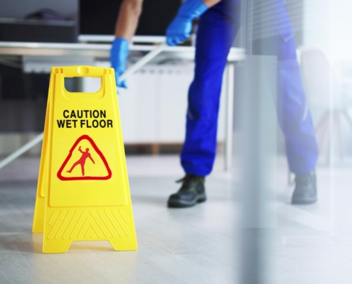 Front view of a wet floor sign with a custodian behind it