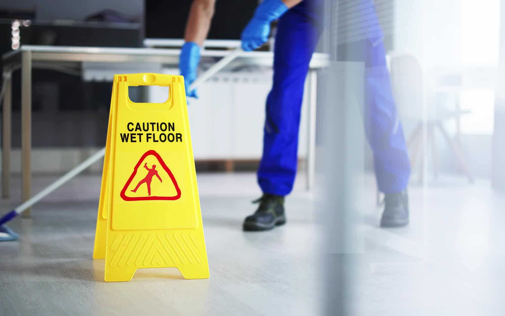 Front view of a wet floor sign with a custodian behind it