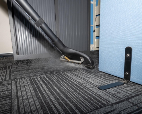 Person steam cleaning carpet in commercial building