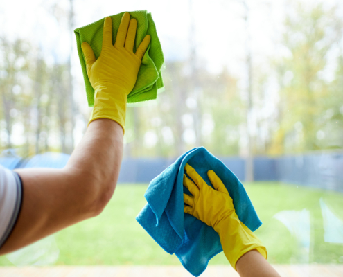 Closeup of cleaners holding rags, wearing yellow rubber gloves. Cleaning glass of window
