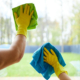 Closeup of cleaners holding rags, wearing yellow rubber gloves. Cleaning glass of window