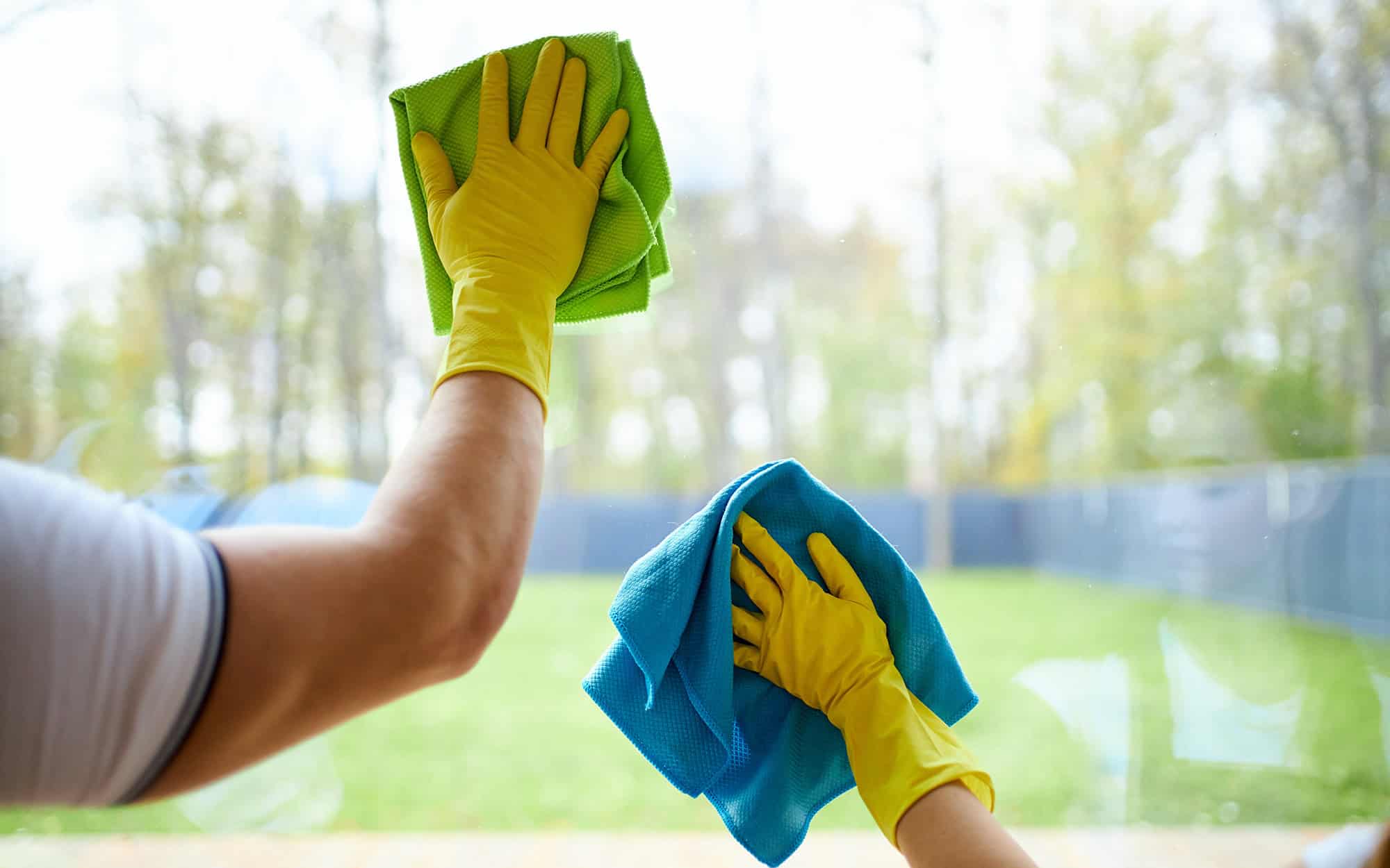 Closeup of cleaners holding rags, wearing yellow rubber gloves. Cleaning glass of window